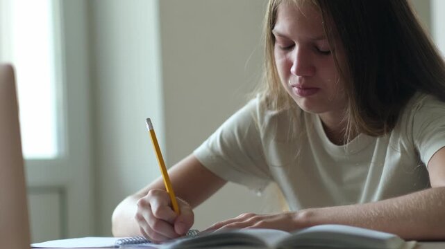 Bored and tired teenage girl crying while doing homework. Schoolgirl unhappy in her studying