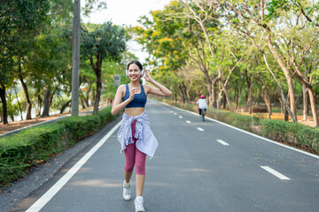 Obraz premium Asian sportswoman wearing headphones while running exercise in garden.