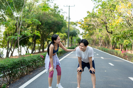 Asian young couple doing morning exercise together outdoors in garden. Attractive man and woman feel happy and relax, practice workout for health care activity in park during sunrise after wake up.
