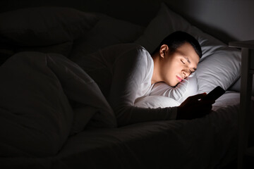 Fototapeta premium Young man with mobile phone sleeping in bed at night