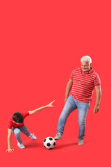 Obraz premium Little boy with his grandfather playing football on red background