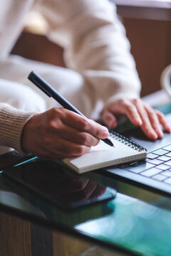 Vertical closeup image of a woman writing on a notebook while working on laptop computer