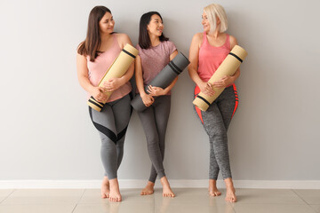 Fototapeta premium Sporty women with fitness mats near light wall