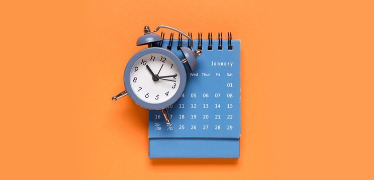 Blue alarm clock on January calendar with orange background