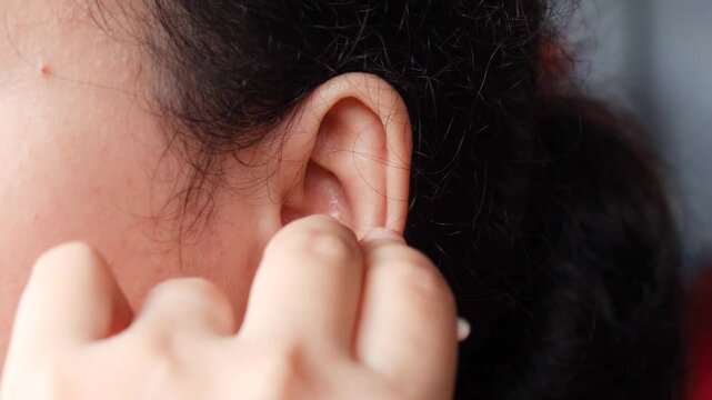 Close up of a young Asian woman cleaning her ear with a cotton swab for personal healthcare and ear disease prevention.