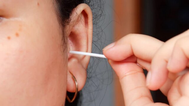 Close up of a young Asian woman cleaning her ear with a cotton swab for personal healthcare and ear disease prevention.