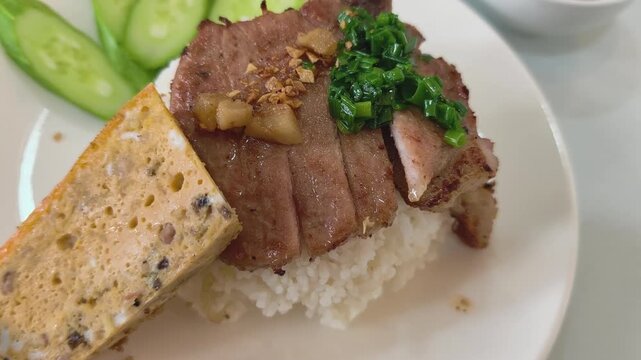 Close-up top down view of a plate of Vietnamese broken rice with grilled pork chop, egg meatloaf, and cucumber
