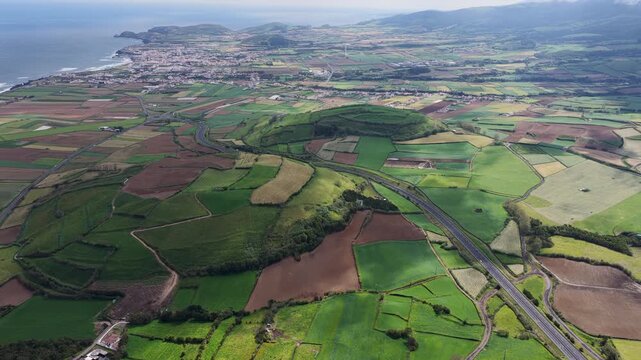 Aerial view of the lush green agricultural fields and rolling hills surrounding the coastal town of Rabo de Peixe, Acores, Portugal.
