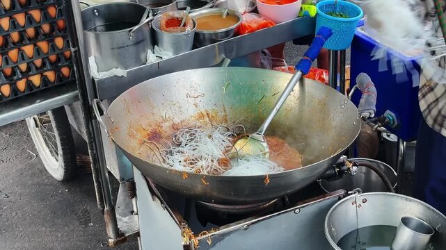 Close up of chef stirring and frying noodles with bean sprouts in a giant wok, authentic Thai street food.