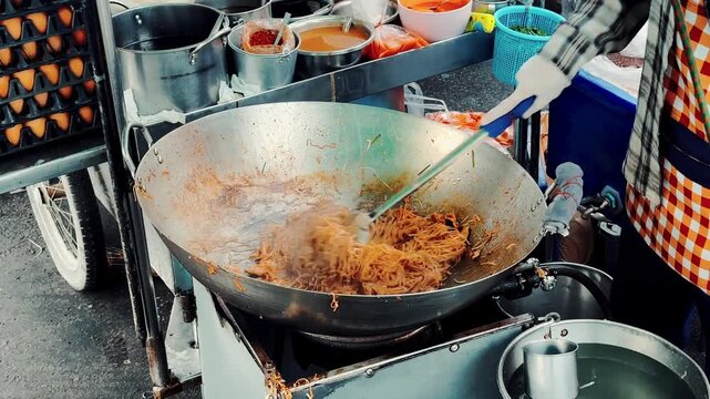 Close up of chef stirring and frying noodles with bean sprouts in a giant wok, authentic Thai street food.