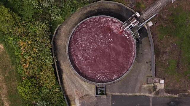Aerial view of a large circular industrial tank filled with dark liquid asphalt, featuring a conveyor belt system, situated in an industrial facility in Rabo de Peixe, Acores, Portugal.