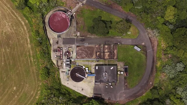 Aerial view of a wastewater treatment facility with circular sedimentation tanks and aeration basins surrounded by lush green vegetation in Rabo de Peixe, Acores, Portugal.