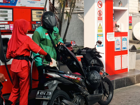 Depok, Idonesia - 06282026: (title/description) A female attendant in red uniform refuels a delivery driver's motorcycle at a Pertamina station, showcasing daily urban logistics.