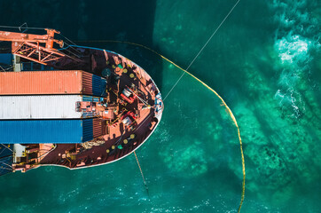 Aerial view of a container cargo ship stands aground after a storm with floating boom around the ship to prevent the spread of petroleum. Top down view of a ship bow © Evgenii Bakhchev