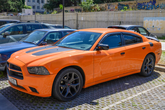 June 28, 2026, Tbilisi, Georgia a calm side view of a parked dodge charger in an urban parking lot with concrete walls and graffiti, showcasing its sleek design and vibrant orange color against