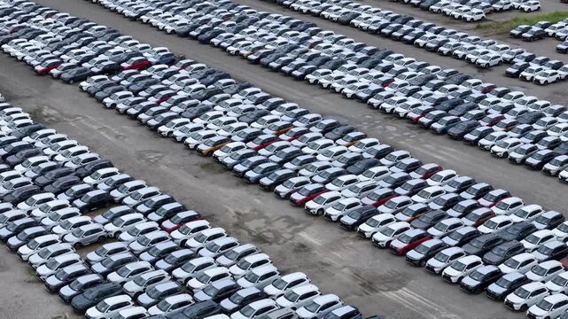 Aerial view of a massive car storage facility showcasing organized rows of new automobiles awaiting international shipment and distribution aerial drone shot