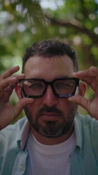 Bearded man putting on eyeglasses outdoors