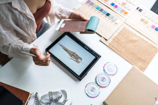 Asian woman fashion designer using tablet for digital clothing sketch digital technology creativity innovation lifestyle in fashion studio.