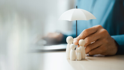 Business hand holding an umbrella above wooden family figures, symbolizing life insurance,...