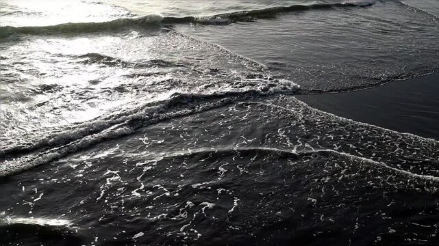 Splash of waves. Black sand beach in Japan with white sea foam patterns and gentle waves rolling onto the shore. Natural coastal texture for travel, ocean, nature and atmospheric background themes.