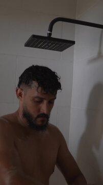 Bearded male person taking shower and cleansing skin