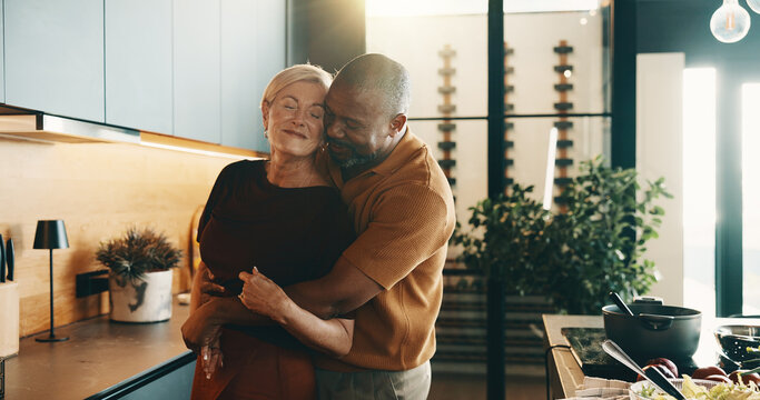 Happy, hug and couple in kitchen for cooking, bonding and love with music, song and meal prep. Interracial, marriage and mature man and woman dancing together for dinner, lunch and embrace in home