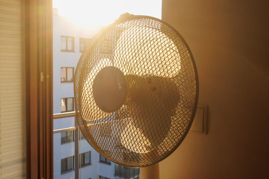 An electric fan standing inside a room at sunrise on a hot summer morning, circulating cool air to improve ventilation during an extreme heatwave.
