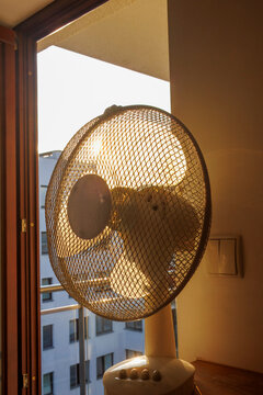 An electric fan standing inside a room at sunrise on a hot summer morning, circulating cool air to improve ventilation during an extreme heatwave.