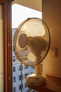 An electric fan standing inside a room at sunrise on a hot summer morning, circulating cool air to improve ventilation during an extreme heatwave.