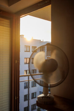 An electric fan standing inside a room at sunrise on a hot summer morning, circulating cool air to improve ventilation during an extreme heatwave.
