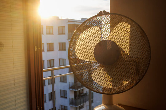 An electric fan standing inside a room at sunrise on a hot summer morning, circulating cool air to improve ventilation during an extreme heatwave.