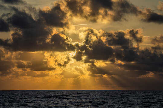View of sunrise over the Atlantic Ocean with golden light filtering through dramatic clouds above the horizon in the United States.