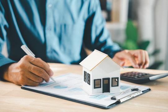 Real estate contract property mortgage finance signing approved, client signs home buying insurance document near homeowner tenant investment papers, calculator and house model on desk