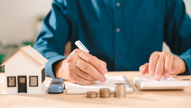 Financial real estate insurance mortgage investment family wealth property ownership vehicle planning shows person using calculator near house model and coin stacks for monthly savings
