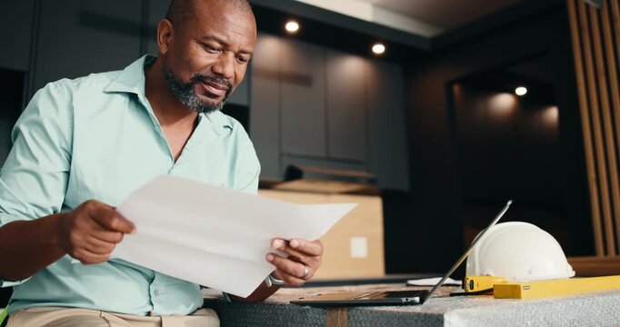 Architect, laptop or black man with paperwork for building plan, safety or maintenance in home. Male person, civil engineer or mature contractor on computer for architecture development or inspection