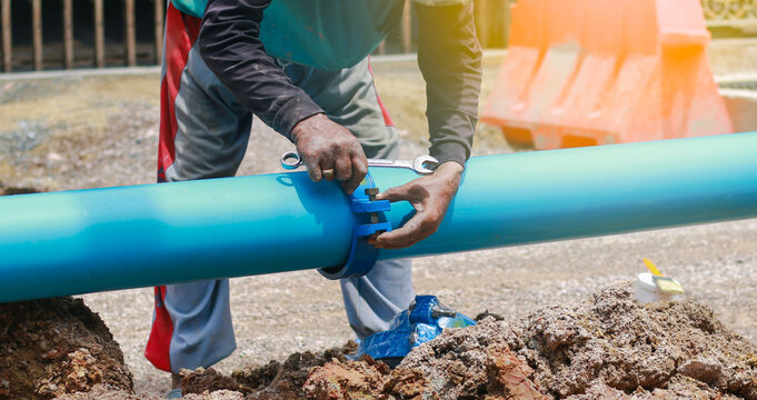 Construction worker or plumber using a wrench to fix a blue PVC water pipe connection. Professional plumbing repair and pipe installation in a city street trench. Industrial utility work.