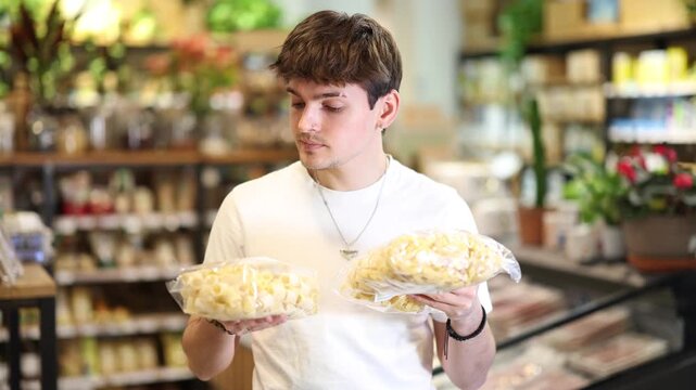  Young guy buyer chooses pasta in package in organic grocery store