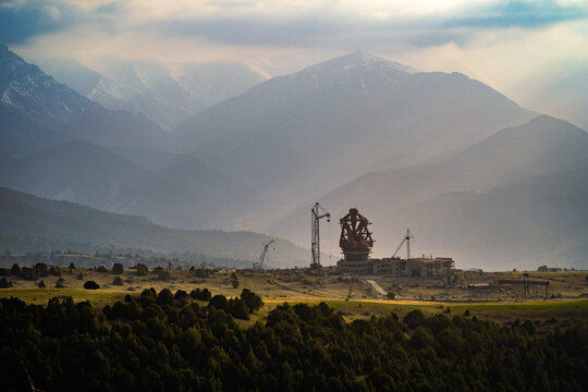 View of the Suffa Radio Observatory under construction with large cranes set against a backdrop of majestic mountains in Zaamin, Jizzakh Region, Uzbekistan.