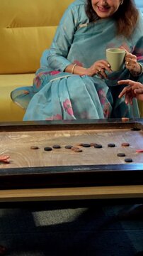 Indian kid playing carrom with grandparents in modern home indoors, elderly grandmother and grandfather enjoying board game with child, family bonding, traditional Indian lifestyle, fun, joy