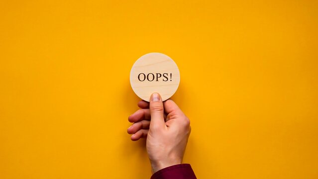 Hand holding oops speech bubble on yellow background with copy space