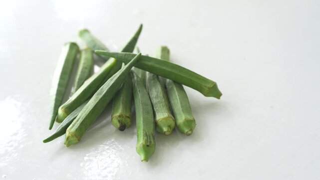 Fresh green okra pods placed on a clean white surface, showcasing natural freshness and healthy vegetable ingredients. Ideal for concepts of home cooking, nutrition, organic produce, and agriculture
