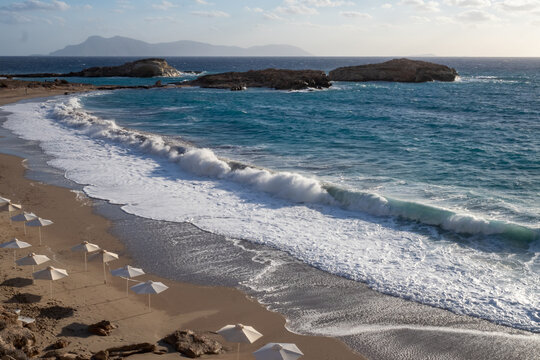 Beach with waves and empty umbrellas on the shore. Karpathos island Lefkos, Greece