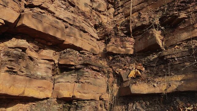 Slow jib down movement revealing the intersecting corner of a weathered escarpment featuring stratified deposits vertical crevices hanging roots and rugged natural landforms