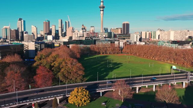 AUCKLAND, NEW ZEALAND, 27 June 2026 &ndash; An aerial view shows the Sky Tower and city skyline overlooking a rugby field with players practicing and cars driving on a highway below.
