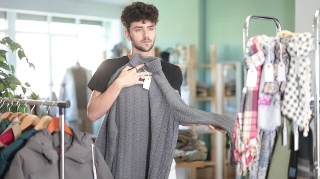 Selective young man choosing some pullover during shopping in retail outlet. High quality 4k footage