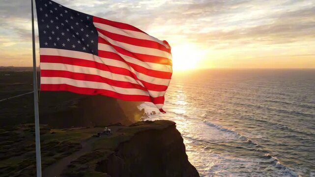 USA Independence Day celebration with American flag waving on cliff overlooking ocean at sunset