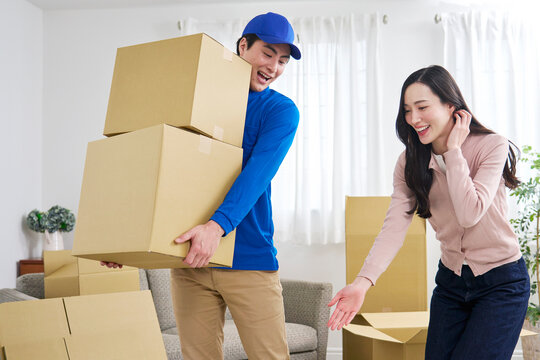 段ボールを持つ引っ越し業者と笑顔で指示する女性