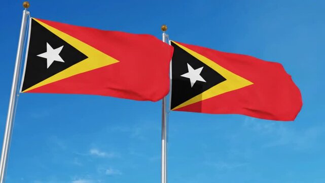 Two flags of east timor waving against a clear blue sky, featuring the red field with black and yellow triangles and a white star