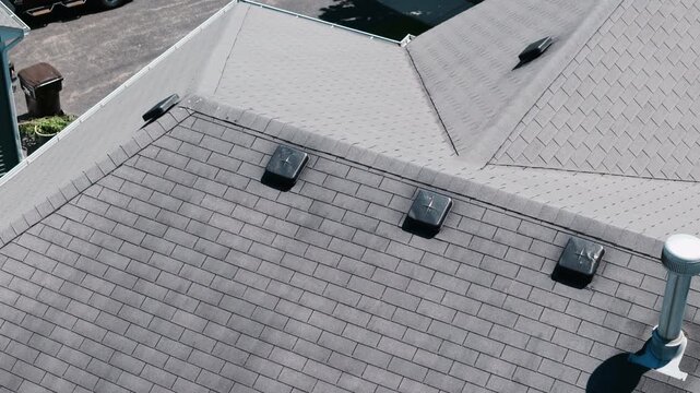 Aerial Drone shoot of a residential house roof with asphalt shingles, roof vents, and modern roofing construction in a suburban neighborhood.