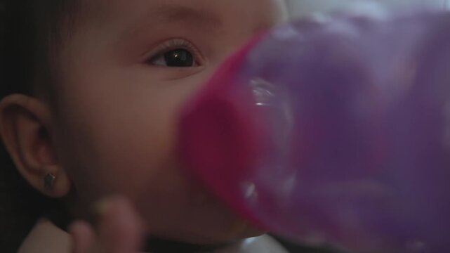 Extreme close-up of a baby drinking water from a purple sippy cup, ideal for infant care, hydration, feeding routines and parenting lifestyle themes.